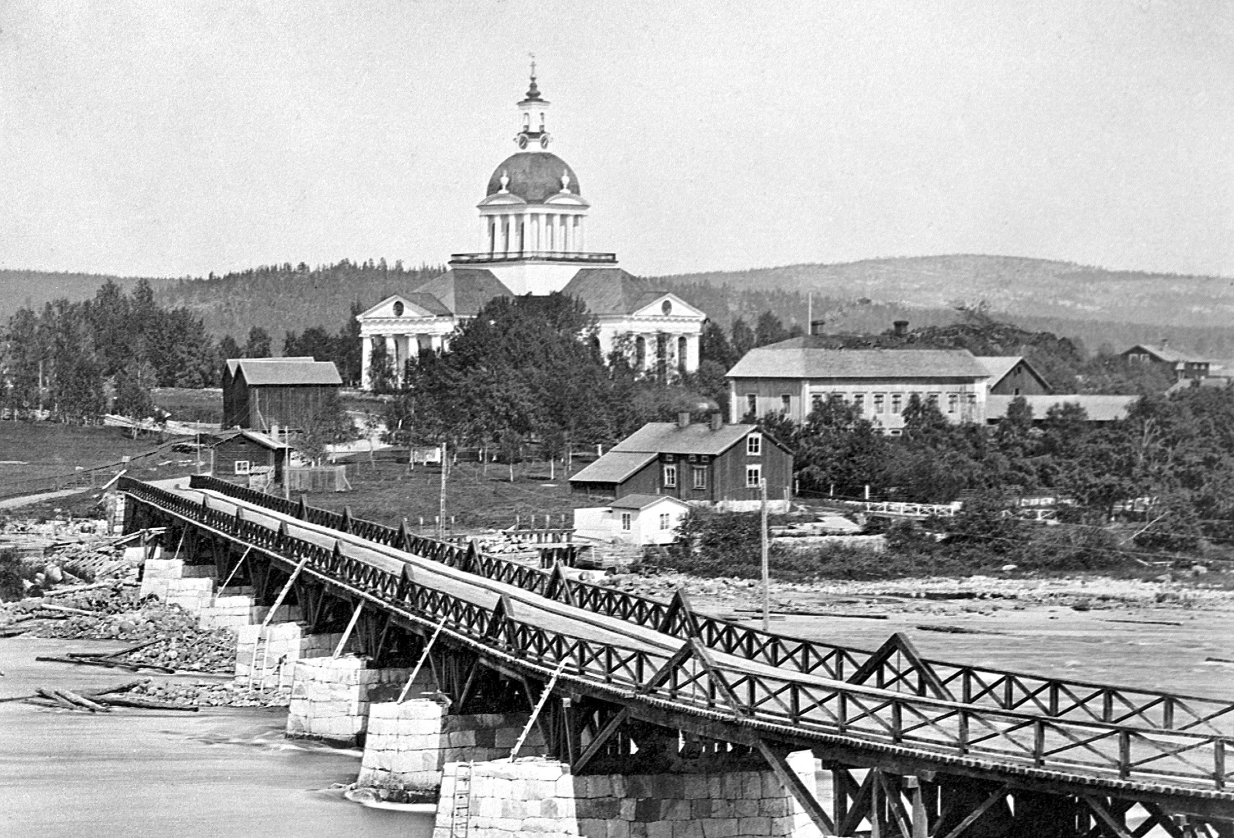 Storbron på 1870-talet med de nya stenfundamenten och bärverk av diagonala bjälkar. Brostugan finns här fortfarande kvar vid brons norra ände, och vägen svänger in mellan tiondebodarna och kyrkan. Foto: Okänd fotograf/Skellefteå museum. 