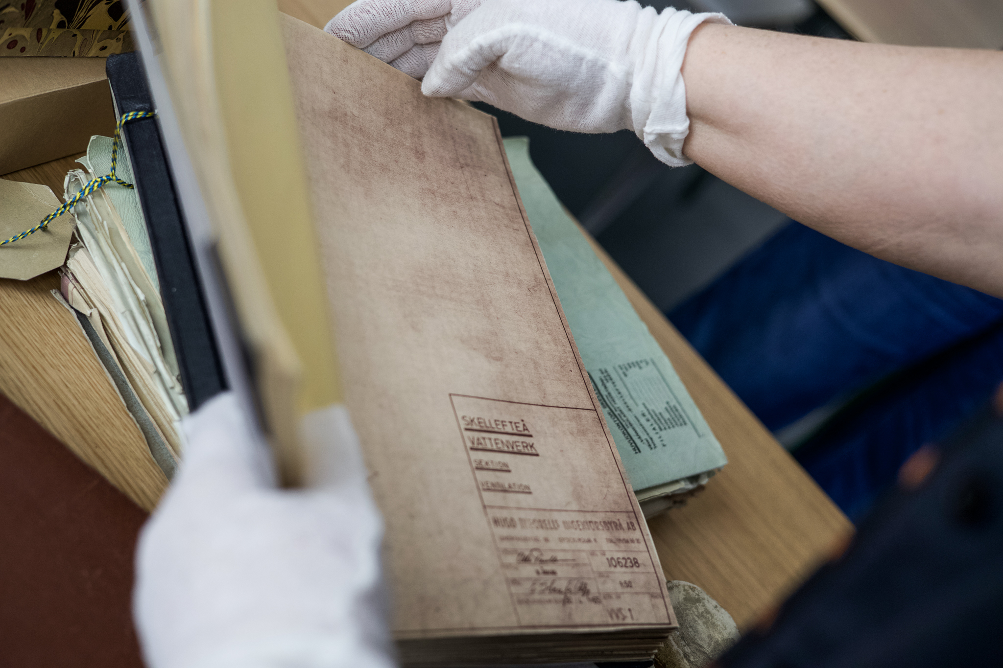 Närbild på händer med vita hanskar som hanterar arkivmaterial